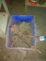 Blue bin containing assorted metal pipes and a pipe threader tool with red handles, covered in dust and showing signs of heavy use.