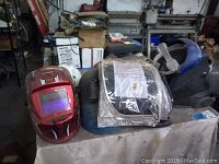 Wide view of the helmets and visors on a table, showing red, blue, black helmets and visors in plastic packaging.