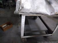 Side angle showing table legs, metal frame, and caster wheel under worn fabric covering surface.