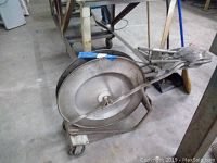 Wide view of steel manual banding bander with large 24 inch spool on wheeled frame, showing handle and frame construction