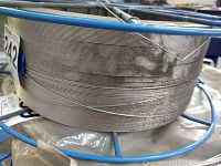 Side view of large coil of tightly wound stainless steel welding wire on blue metal spool frame showing wire thickness and spool structure.