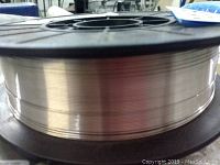 Close-up of spool showing shiny stainless steel wire wound on black plastic reel.