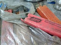 Photo showing Arcair branded red boxes labeled Copperclad Point Electrodes containing copper-coated gouging carbon electrodes and some loose rods in a plastic bag.