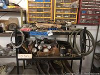 Photo of metal shelf with pressure gauges and assorted tools and fittings. Coiled hoses on side and pipe wrenches below.