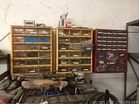 Three plastic wall-mounted storage units with small drawers filled with metal hardware items including bolts, nuts, washers, and fittings.