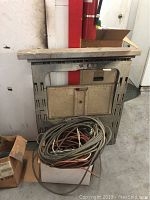 Saw horse leaning against wall with extension cords coiled on ground in front.