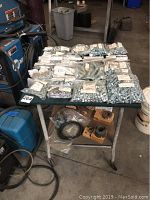 Photo showing multiple small plastic bags of galvanized bolts, nuts, and washers arranged on a small metal cart in a workshop environment.