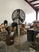 Full view of industrial standing fan and surrounding shop chairs and equipment in warehouse environment