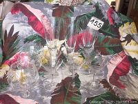 Full display of nine pieces glassware with bamboo etching, three talle pilsners, three snifters, and six small champagne glasses, arranged on patterned fabric.