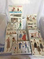Photo showing a collection of vintage sewing pattern envelopes stacked and laid out, featuring Vogue, McCall's, and Butterick brand patterns with illustrated women's clothing designs.
