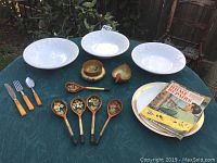 Three white 10.5-inch serving bowls, Russian lacquerware spoons and small containers, La Quinta Palm Springs Hotel dinner plate, mid-century Home Repair Guide book on outdoor table