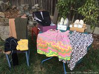 Full lot showing various clothing items on chairs and table, multiple pairs of shoes on top boxes, and colorful skirt item