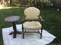 Vintage upholstered wooden chair with patterned fabric and wooden side table shown outdoors on grass with a white blanket underneath.