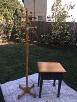 Photo showing the full wooden coat rack with eight pegs next to the wooden side table on a grass lawn with a white blanket underneath.
