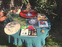 Photo of Mexican tin Christmas tree candelabra on red base, gold and silver placemats, holiday napkins and plates including snowman and Santa designs, boxed 'Ornagami' Christmas tree shaped lights untested, and assorted small Christmas ornaments arranged on a green table.