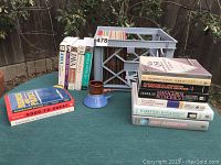 Overview photo showing all books, filing crate with colored folders, and vintage ceramic mug on green outdoor table.