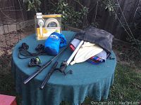 View of all items on green table with fishing rods, oars, hammock, rope and boxed handheld shower