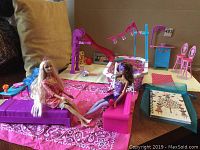 Full view of two Barbie dolls seated on pink furniture with the pool playset and other furniture surrounding them