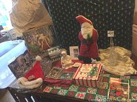 Photo showing assortment of vintage and new Christmas decor including Virgin Mary figurine, stuffed Santa, Santa hat, advent calendars, Christmas cards, gift box, fabric pieces, and glass evergreen tree.