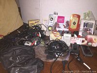 Photo showing an assortment of electronic devices on a table including flip phones, cables, batteries, smoke alarm box, and other packaged electronic components.