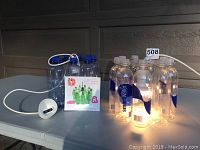 Two plastic bottle chandelier fixtures displayed on a flat surface, one illuminated showing the glowing bottles.