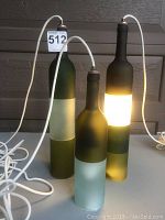 Three green frosted wine bottle hanging light fixtures with frosted and pearl cut bottle sections visible, all plugged in and illuminated to show working condition