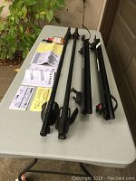 Full overview of two metal crossbars and two bike tray attachments laid out on a table with instruction manuals and lock set.