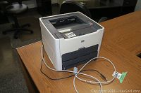 Front view of HP LaserJet 1320 printer showing control panel, paper tray, and cables attached, displaying model plate for HP49A cartridge use.