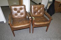 Frontal view of the two brown vinyl office chairs showing seat, backrest, and wooden armrests.