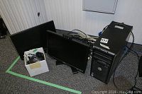 Dell desktop computer tower and two Dell monitors with a white box containing cables and mice, all sitting on carpeted floor.