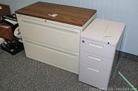 Two file cabinets side by side, lateral cabinet with faux wood top and smaller metal cabinet visible showing condition and size.