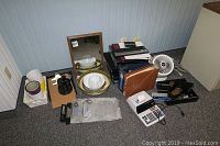 View of all assorted office supplies including calculator, fans, binders, clipboards, bowls, planters, hole punch, mirror, and paper cutter arranged on carpeted floor.