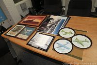 Photo showing framed posters and prints on a table including airplane silhouette, technical diagrams, and round plates with airplane illustrations.