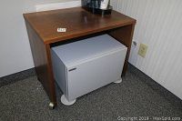 Wooden table with flat top and a grey Sharp metal cabinet underneath it, placed on carpet