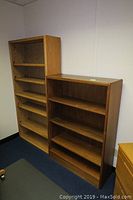 Two wooden bookshelves shown side by side from a corner view illustrating height and shelving configuration