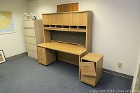 Large office desk with removable hutch and file cabinet placed on the right side. Desk has three drawers with the top drawer missing a screw. Desk and hutch have a light wood finish.