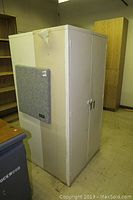White metal storage cabinet featuring a fabric Clearsonic pin board attached on the side, showing wear and chipped paint.