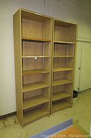 Front view of two tall wooden bookshelves with six shelves each, against a white wall in a room with tiled floor.
