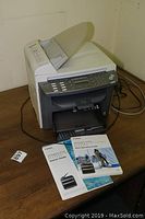 Photo of Canon ImageCLASS MF4350d multifunction printer positioned on a wooden surface with visible power and USB cables, showing numeric keypad and display screen.