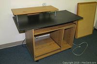 Computer desk side view showing wood grain lower shelving, open compartments, black laminate top, and elevated printer shelf