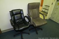 Two office chairs side by side in an office setting: one black padded chair and one taupe padded chair showing arm wear.