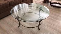 Full view of round glass-top coffee table with metal frame in a living room setting next to a sofa.
