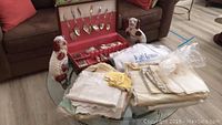 Photo of the entire lot showing the silverware set in red box, assorted folded table linens, and the two ceramic dog statues on the sides.