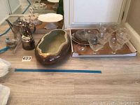 Photo of vintage Palm Silver tea pot, serving items, decorative pot, divided glass serving dish, and glass ice cream dishes lined in cardboard box.
