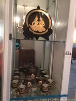 Photo of Asian tea set with teapot, sugar bowl, creamer, six cups and saucers inside a glass display cabinet.