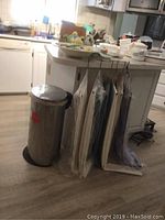 Wide view of kitchen island with several hanging tablecloths on hangers and a trash can next to the island.