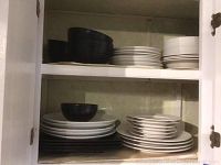 Open cabinet showing stacks of black and white dinner plates, salad plates, and black bowls with red interiors.