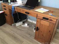 Full view of the wooden desk featuring a flat work surface, three drawers with black handles, and a left and right side arrangement with a cabinet door on the right side.