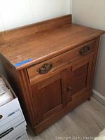 Wooden filing cabinet showing its top, drawer with decorative handle, and double doors below with shelf inside.
