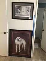 Two framed dog art pieces on white wall: one smaller black and white print of three dogs in outdoor setting, one larger colored print of a single white dog.